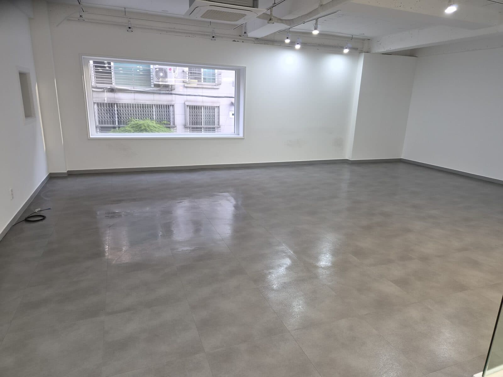 가구가 들어오기 전 빈 사무실. 흰 벽과 회색 타일 바닥, 천장 트랙 조명만 있다.